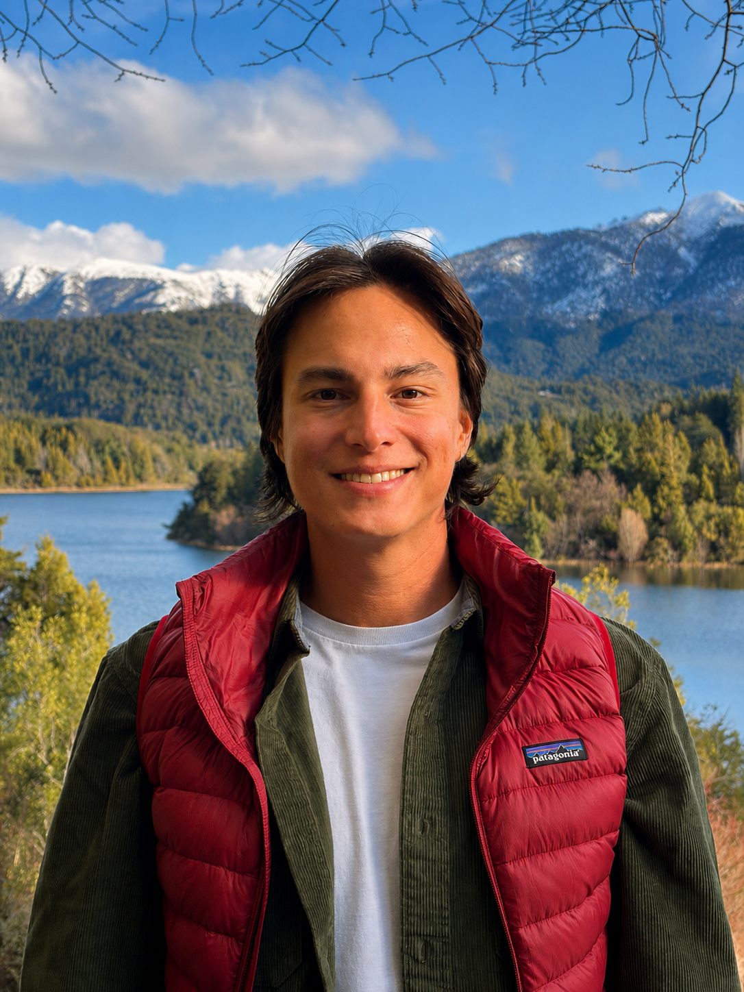 Portrait of Lubin wearing a red vest beside a mountain lake